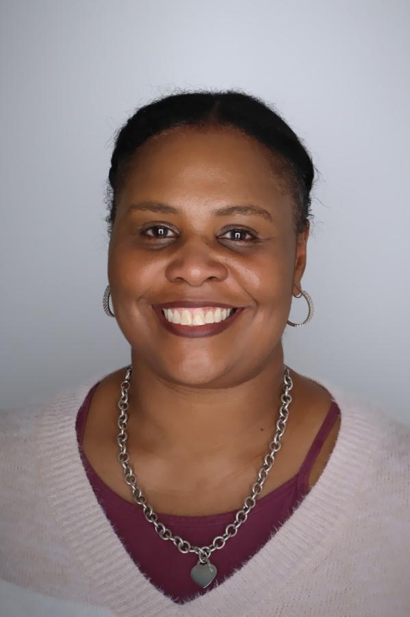 Executive Director Nicole Green smiling at the camera wearing a purple shirt in front of a grey background